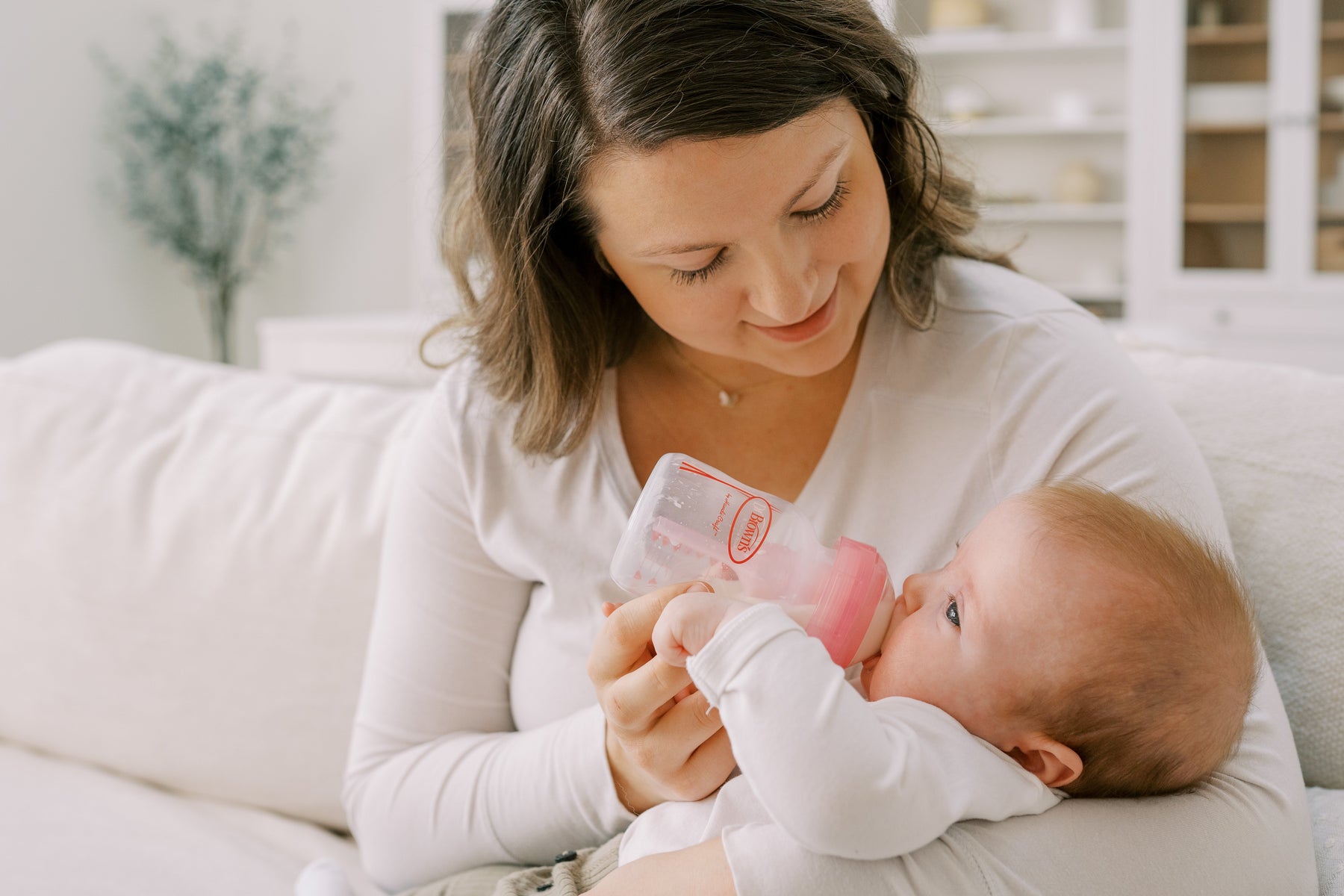 “Mother gently feeding baby with Dr Brown’s anti-colic wide-neck bottle in natural light.